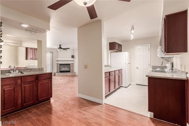 kitchen with ceiling fan, white appliances, a tiled fireplace, and sink