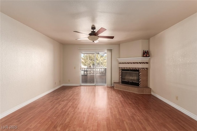 unfurnished living room with hardwood / wood-style floors, a tile fireplace, and ceiling fan