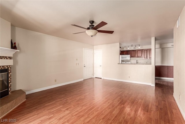 unfurnished living room featuring a brick fireplace, track lighting, dark hardwood / wood-style floors, and ceiling fan