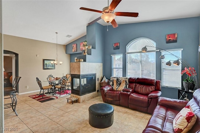 tiled living room featuring a fireplace, ceiling fan with notable chandelier, and vaulted ceiling