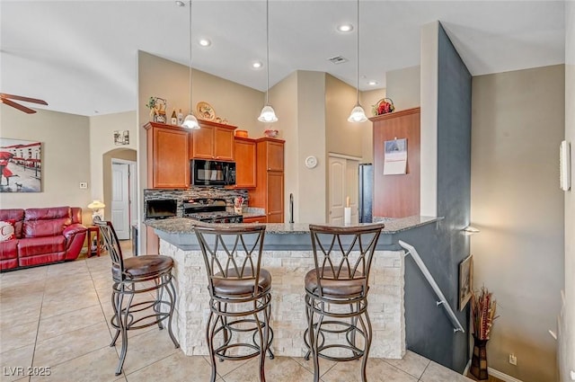 kitchen featuring stone countertops, decorative light fixtures, a breakfast bar area, and range