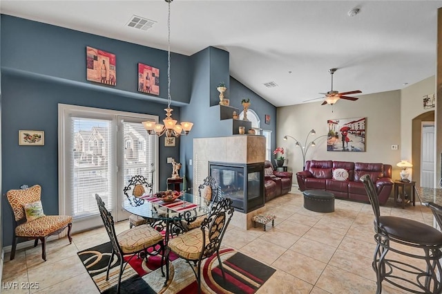 tiled dining room featuring lofted ceiling, ceiling fan with notable chandelier, and a tile fireplace