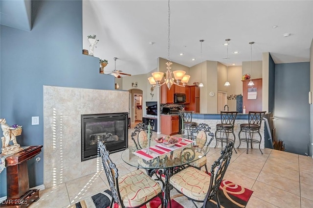 tiled dining area featuring ceiling fan with notable chandelier and a fireplace