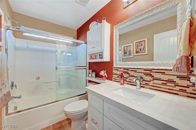 full bathroom featuring hardwood / wood-style floors, backsplash, shower / bath combination with glass door, vanity, and toilet