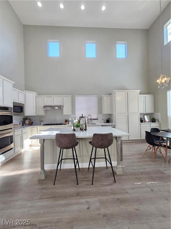 kitchen featuring a kitchen bar, white cabinetry, a center island, hanging light fixtures, and stainless steel appliances