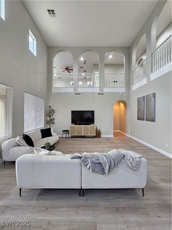 living room featuring a towering ceiling, wood-type flooring, and ceiling fan