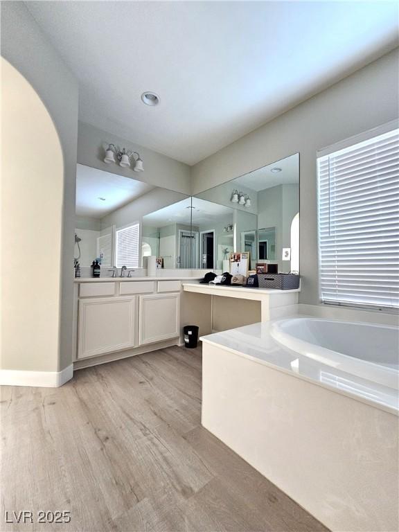 bathroom featuring a healthy amount of sunlight, vanity, a bath, and wood-type flooring