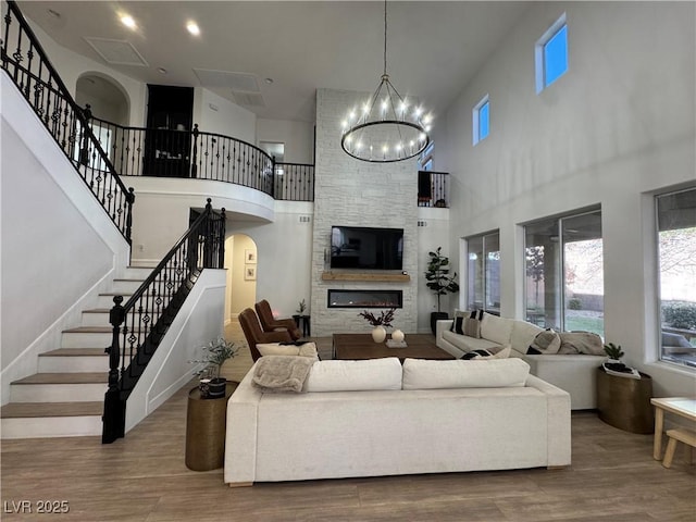 living room featuring a large fireplace, wood-type flooring, a chandelier, and a towering ceiling