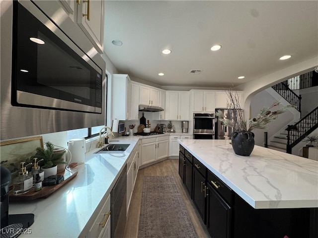 kitchen with a kitchen island, hardwood / wood-style floors, sink, white cabinets, and stainless steel appliances