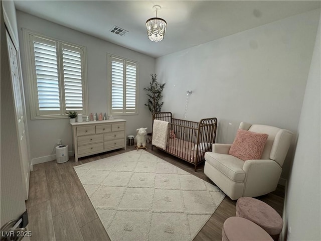 bedroom featuring a crib, hardwood / wood-style floors, and a notable chandelier