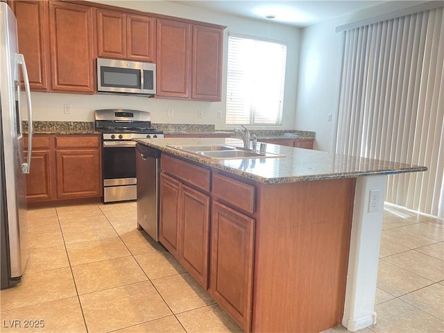 kitchen with sink, stone countertops, light tile patterned floors, an island with sink, and stainless steel appliances