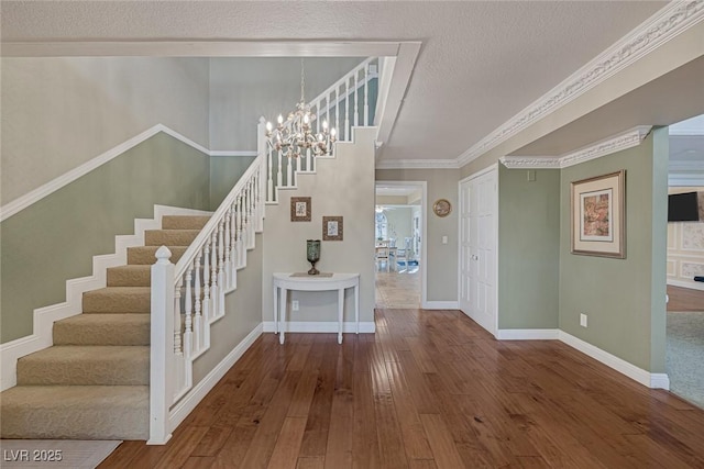 foyer with ornamental molding, wood-type flooring, a textured ceiling, and a notable chandelier