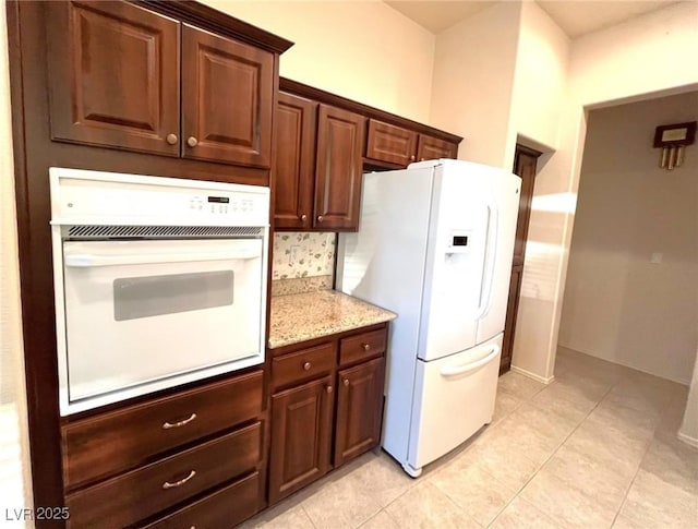 kitchen featuring light tile patterned flooring, white appliances, and light stone countertops