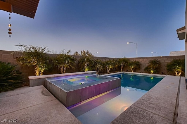 pool at dusk featuring an in ground hot tub and a patio