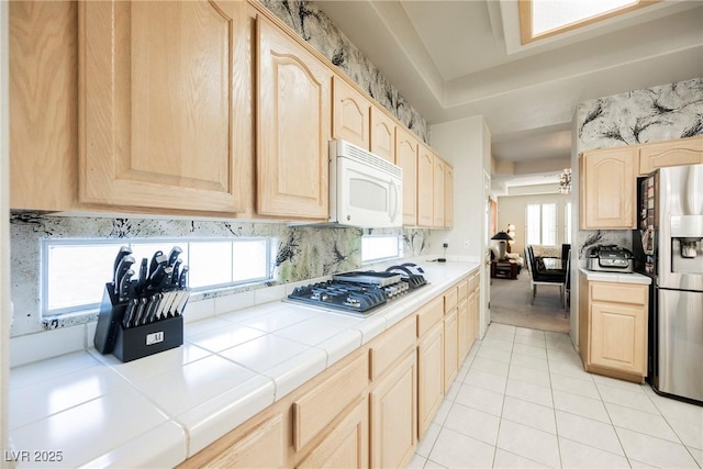 kitchen with light brown cabinetry, tasteful backsplash, tile counters, light tile patterned floors, and stainless steel appliances