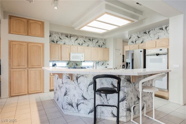 kitchen featuring a kitchen breakfast bar, tile counters, and white appliances