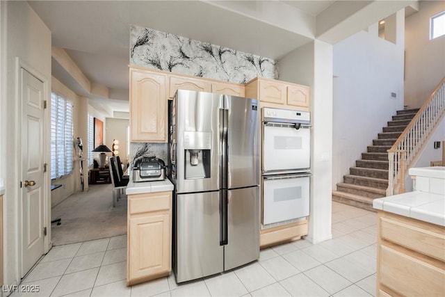 kitchen featuring double oven, tile countertops, light brown cabinets, and stainless steel refrigerator with ice dispenser