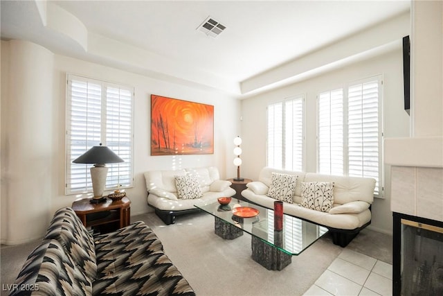 tiled living room featuring a tiled fireplace, a tray ceiling, and plenty of natural light