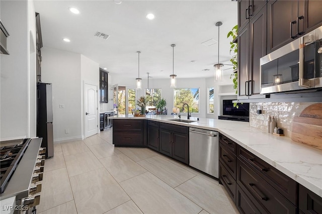 kitchen featuring appliances with stainless steel finishes, decorative light fixtures, sink, light stone counters, and kitchen peninsula