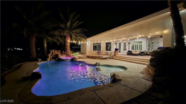 pool at night with an in ground hot tub and a patio area