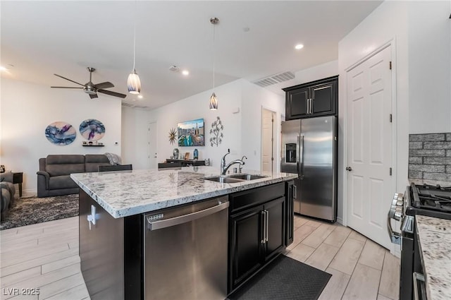 kitchen with sink, hanging light fixtures, ceiling fan, stainless steel appliances, and a center island with sink