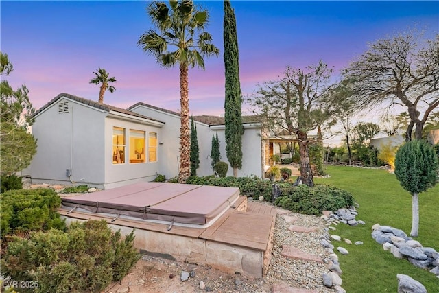 back house at dusk featuring a lawn and a covered hot tub