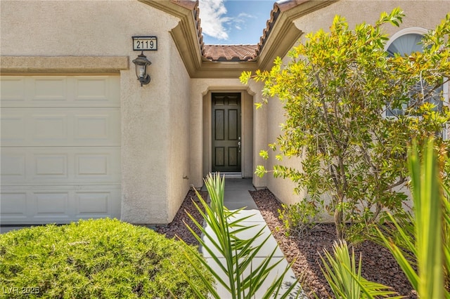 property entrance featuring a garage, stucco siding, and a tiled roof