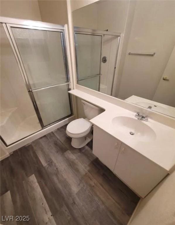 bathroom with hardwood / wood-style flooring, vanity, toilet, and a shower with shower door