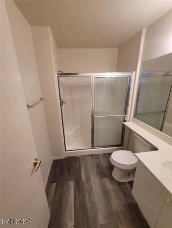 bathroom with hardwood / wood-style flooring, vanity, a shower with door, and toilet