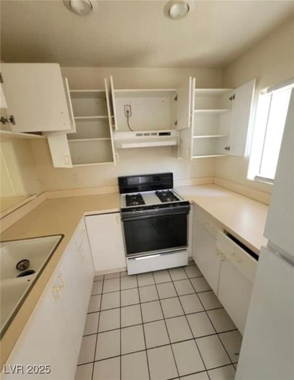 kitchen with sink, light tile patterned flooring, white cabinets, and white stove