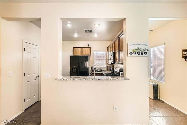 kitchen with kitchen peninsula, sink, light stone countertops, and black appliances