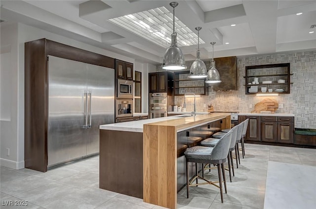 kitchen featuring pendant lighting, sink, butcher block countertops, built in appliances, and a center island with sink