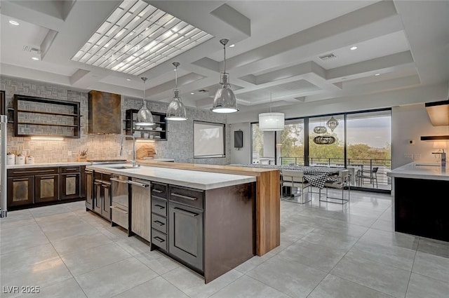 kitchen with decorative light fixtures, tasteful backsplash, coffered ceiling, dark brown cabinets, and a center island with sink