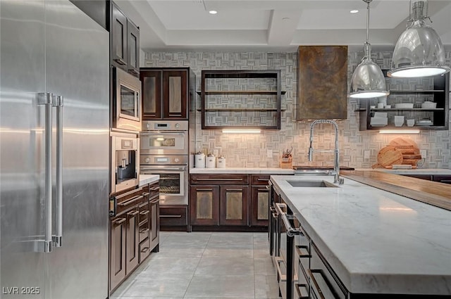 kitchen featuring sink, built in appliances, pendant lighting, light stone countertops, and backsplash