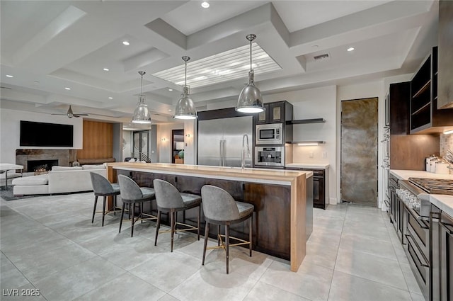 kitchen featuring a breakfast bar, hanging light fixtures, coffered ceiling, a center island, and built in appliances