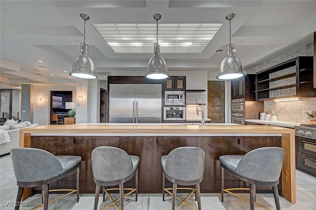 kitchen featuring a kitchen bar, built in appliances, hanging light fixtures, and decorative backsplash