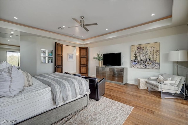 bedroom featuring a raised ceiling, ornamental molding, and light wood-type flooring