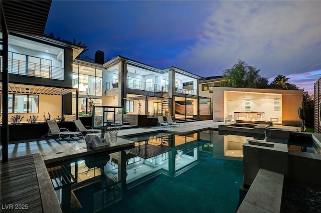 pool at dusk featuring a patio area and exterior kitchen