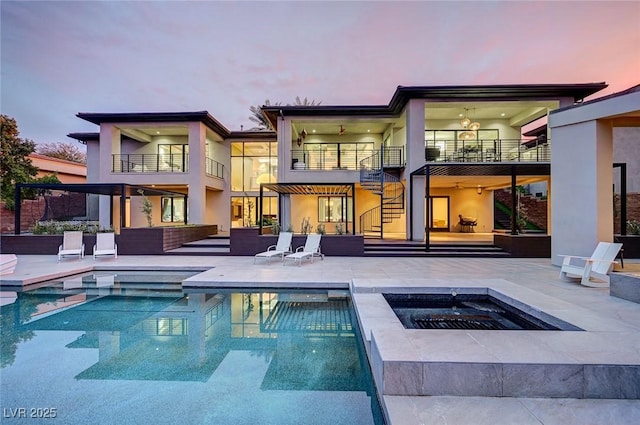 back house at dusk featuring a pool with hot tub, a patio, and a balcony