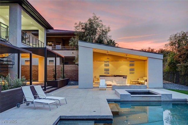 back house at dusk featuring a swimming pool with hot tub, a patio area, and a fire pit