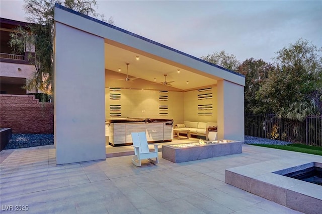 patio terrace at dusk with ceiling fan, a covered hot tub, and a fire pit