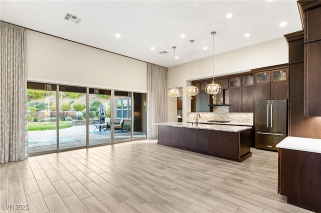 kitchen with high quality fridge, pendant lighting, sink, backsplash, and dark brown cabinets