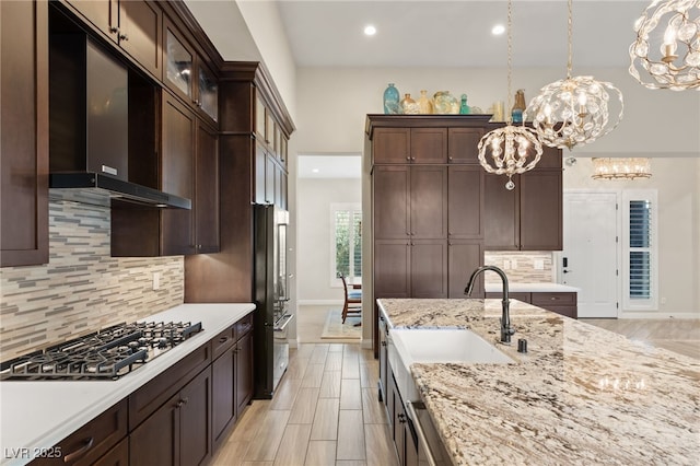 kitchen with pendant lighting, wall chimney range hood, refrigerator, tasteful backsplash, and stainless steel gas stovetop