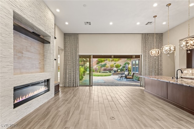 interior space featuring a tiled fireplace, sink, a towering ceiling, and light hardwood / wood-style flooring