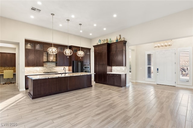 kitchen with pendant lighting, appliances with stainless steel finishes, dark brown cabinets, light hardwood / wood-style floors, and decorative backsplash