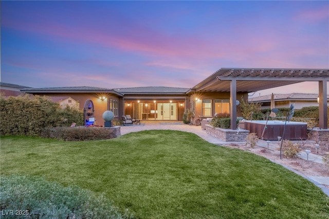 back house at dusk with a hot tub, a pergola, a patio, and a lawn