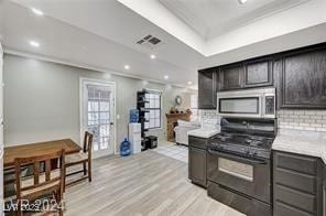 kitchen with a tray ceiling, black gas range, light hardwood / wood-style flooring, and backsplash