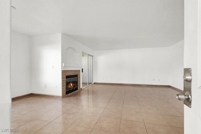 unfurnished living room featuring light tile patterned floors, baseboards, and a tiled fireplace