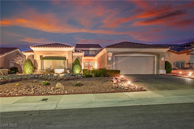 mediterranean / spanish-style house featuring driveway, a tiled roof, a garage, and stucco siding