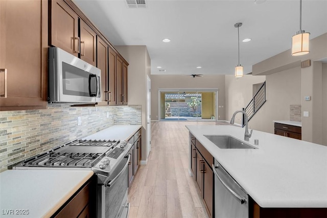 kitchen featuring sink, hanging light fixtures, appliances with stainless steel finishes, light hardwood / wood-style floors, and decorative backsplash